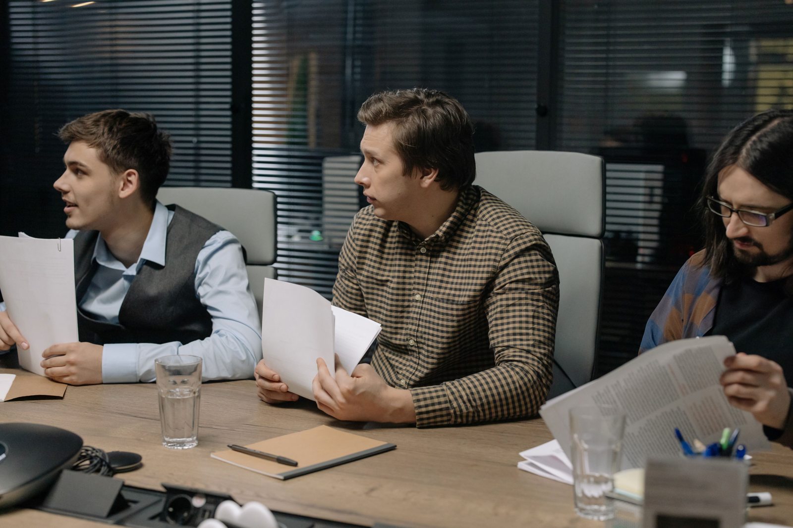 Three people reviewing paper documents around a meeting table